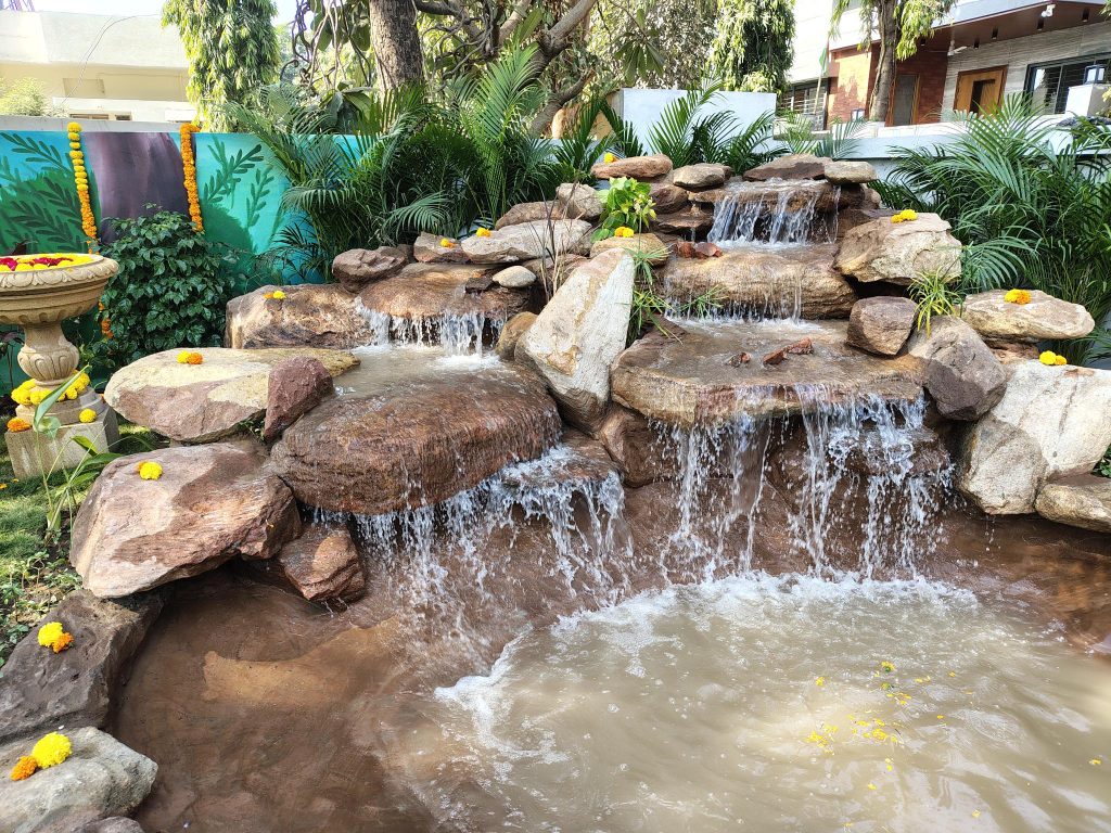 A small waterfall in a garden with rocks and plants at Kalyan Jivashray Foundation.